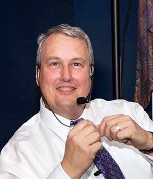 Dr. Randy Ferrance wearing a headset and suit while DJing an event