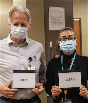 Two InnovAge Employees Wearing Masks And Holding Holding Signs; One Sign Says 'Dirty', One Sign Says 'Clean'