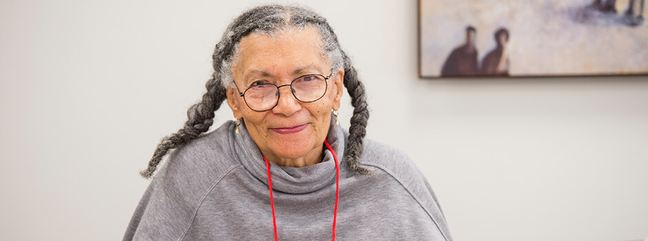 Older woman in glasses writing in a book looking at camera