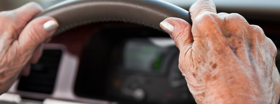 Two elderly hands on the steering wheel of a vehicle