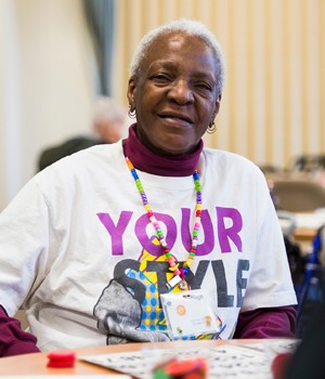 Older Female Adult Sitting At Table Smiling