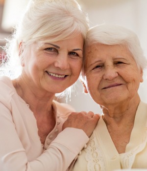 Older mother and daughter smiling with heads together looking at camera
