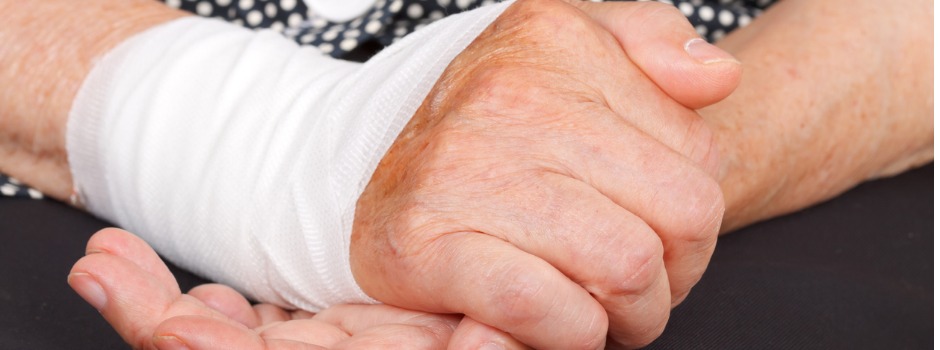 Two older hands clasped together, one is wrapped in a bandage