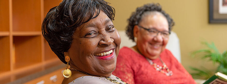 Two smiling PACE participants looking at camera while seated in a library