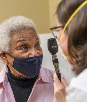Older woman in mask has her eyes checked by a PACE doctor.