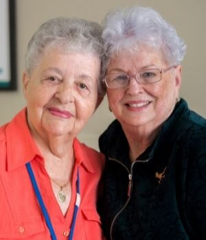 Two older women touching heads, smiling and looking at the camera
